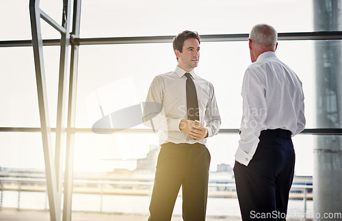 Image of Collaboration, window and flare with business men in discussion while standing in their corporate office. Meeting, teamwork and planning with a corporate employee chatting to a colleague at work