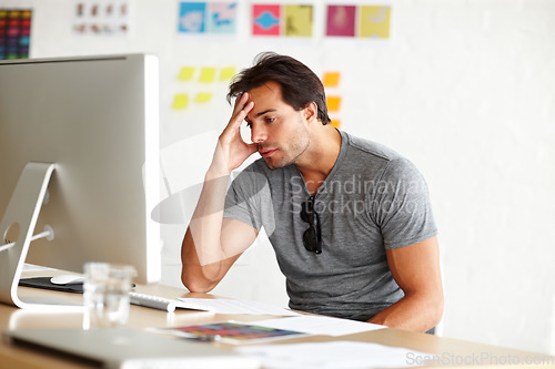 Image of Suffering from writers block. A handsome man sitting at a desk and looking at a computer screen with head rested on his hand.