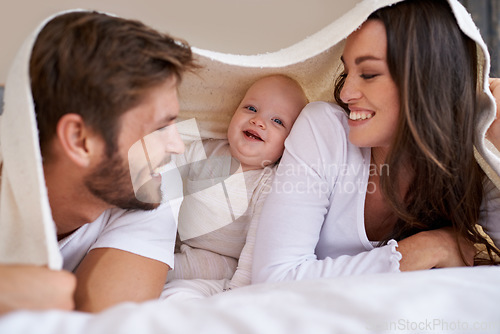 Image of Happy mother, father and baby with blanket on bed for love, care and quality time together. Parents, family and playful newborn child relaxing in bedroom with bedding fort, smile and bonding at home