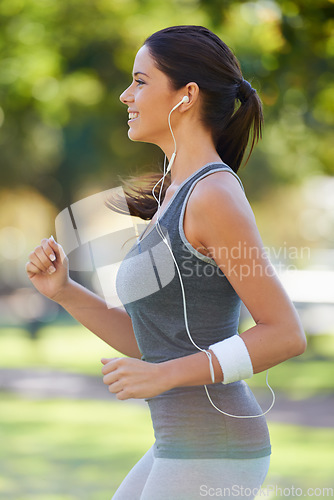 Image of Sports, earphones and athlete running in a park for health, wellness and outdoor exercise. Nature, fitness and female runner doing cardio workout in garden listening to music or radio and training.