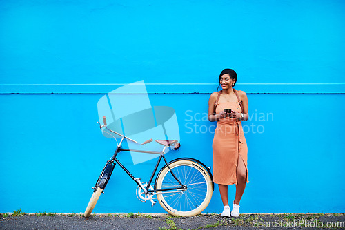 Image of Bicycle, young woman with smartphone and happy outside by blue wall. Cycling in urban area, health wellness and female person on cellphone outdoors standing in streets with bike or cycle in road