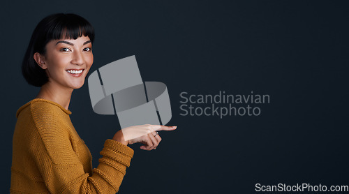 Image of Woman is pointing, marketing and mockup space with portrait, smile and promo isolated on dark background. Young female person, happy ambassador and branding with advertising and show in studio