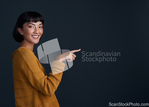 Image of Woman is pointing, advertising and mockup space with portrait, smile and promo isolated on dark background. Happy female person, ambassador and branding with marketing and presentation in studio