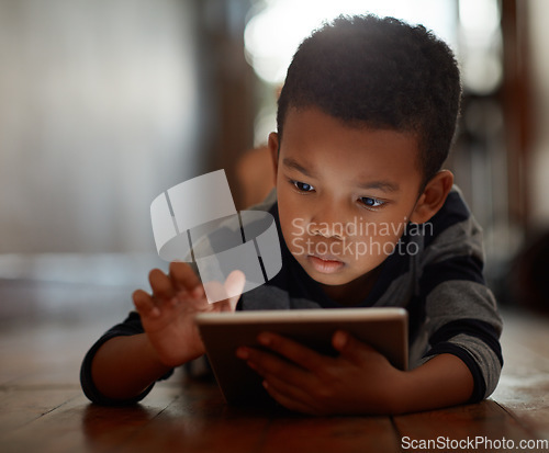 Image of Little boy, browsing and on digital tablet or playing games or streaming video on the internet and lying on the floor at home on bokeh. Technology, device and male child downloading app or reading