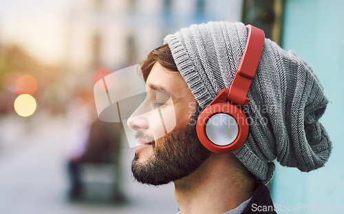 Image of Relax, smile and man with headphones for music, radio or a podcast in the city. Happy, freedom and a young person sitting, enjoying and listening to audio, calm songs or zen sound while downtown