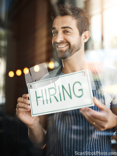 Image of Man with hiring sign, window with job opportunity advertising, happy waiter or barista in portrait. Small business, recruitment and male owner with onboarding, promo poster for new hire at cafe