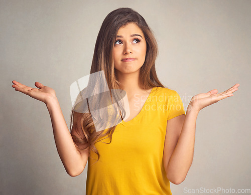 Image of Thinking, doubt and shrug with a woman in studio on a gray background looking confused by her options. Idea, question and hand gesture with an attractive young female person weighing up a decision