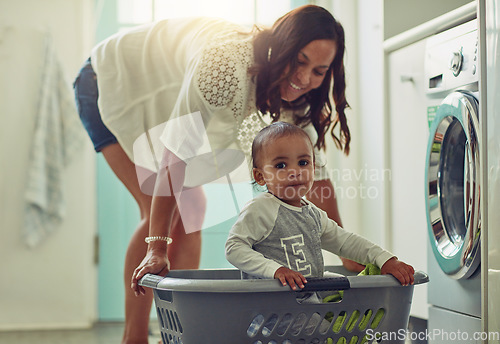 Image of Cleaning, mother and baby playing in basket doing the laundry in their home. Hygiene or clean for wellness, positive and happy family have fun bonding together at washing machine with lens flare