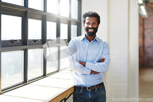 Image of Portrait, window and smile with a business man arms crossed in the office, feeling positive about future success. Mindset, vision and happy with a male employee standing at work during his break