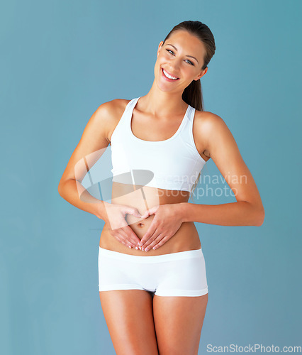 Image of Heart shape, hand gesture on stomach and happy woman in portrait, gut health and wellness isolated on blue background. Weight loss, fitness and healthy female person, self love and bodycare in studio