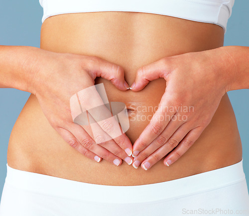 Image of Heart, hands on stomach and woman, gesture and closeup with gut health and wellness isolated on blue background. Weight loss, fitness and healthy female person with self love and body care in studio