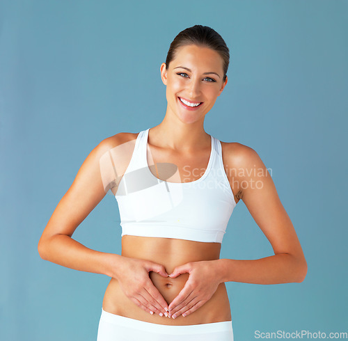 Image of Heart shape, hand gesture on stomach and woman in portrait, gut health and wellness isolated on blue background. Weight loss, fitness and healthy female person with self love and body care in studio