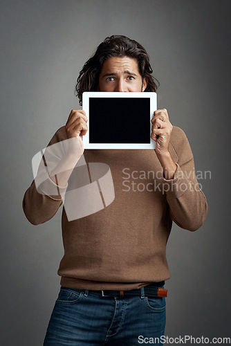 Image of Tablet screen, mockup and portrait of man peeking in studio isolated on a gray background. Touchscreen, scared and male person with space for marketing, advertising and technology for promotion.