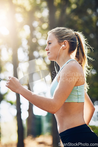 Image of Woman with earphones, running in forest and fitness with music, listening for motivation on run in park. Female runner outdoor, podcast or radio streaming for exercise and health, cardio and energy