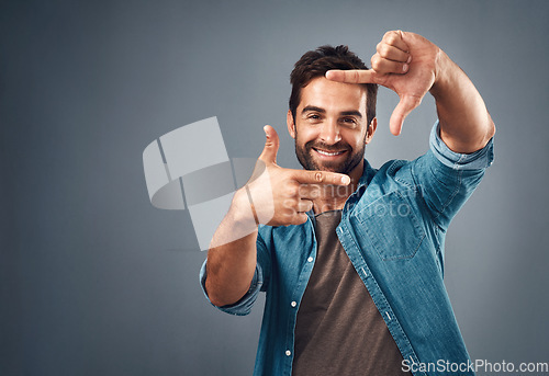 Image of Frame, hands and portrait of man in studio on gray background with happiness, confident and smile. Finger border, mockup and male person face with hand sign for picture, photography and perspective