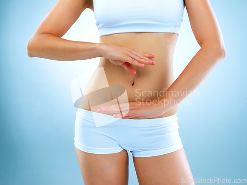 Image of Woman, stomach and body with blue background with hands for diet and exercise for health. Model, fitness and women in studio for digestion diet and workout with weight loss for healthy living.