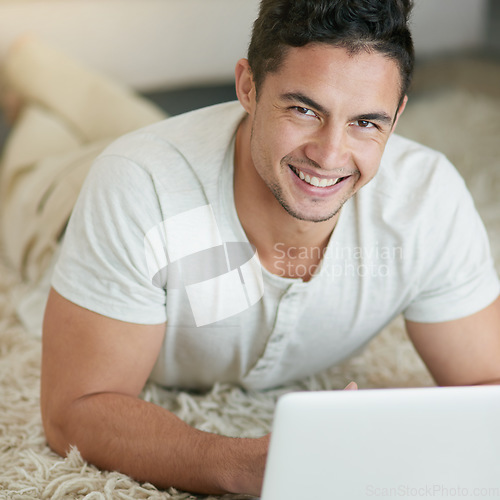 Image of Laptop, relax and portrait of man typing on the floor in his home, house or apartment with smile lying on carpet. ecommerce, happy and young male person or freelancer doing remote work or project