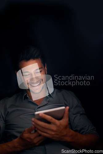 Image of Business man, tablet and night with smile for meme, social media app or comic video on web, internet or blog. Young businessman, digital touchscreen and reading in dark workplace with funny article