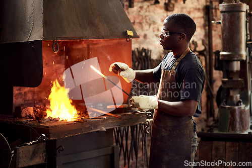 Image of Blacksmith, fire and a black man melting metal in a workshop for manufacturing or industrial design. Factory, welding or industry with a male designer in metalwork using a hot flame to melt material