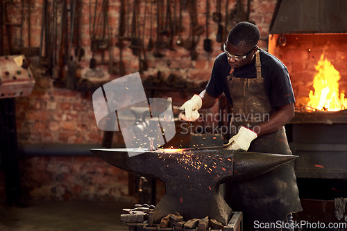 Image of Blacksmith, worker and metal forge in workshop and manual industry working on hot steel with hammer, sparks or fire. Black man, welding or iron tools manufacturing or expert, trade and dark workspace