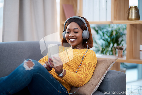 Image of Relax, phone and music with a black woman on a sofa in the living room of her home streaming audio through headphones. Mobile, freedom and time off with a happy young female listening to the radio