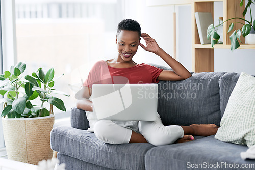 Image of Happy, black woman and relax with laptop on a sofa, comfortable and chilling on the weekend. Streaming, smile and African female person online for internet, search and subscription in a living room