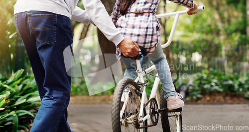 Image of Father teaching his child to ride a bicycle on a path in an outdoor green community park. Love, bonding and closeup of a man helping his girl kid on a bike in garden for fun, exercise and development