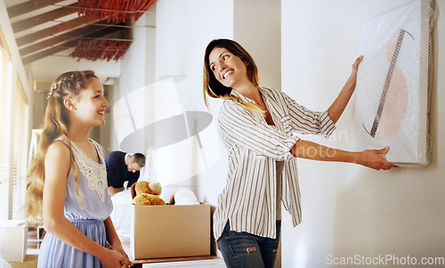 Image of Moving house, property and a girl with her mother hanging a painting in their new home on relocation day. Real estate, family and children with a daughter helping her parent with interior decoration