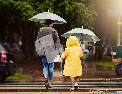 Image of Back, raincoat or umbrella with a mother and daughter walking across a street in the city during winter. Autumn, crosswalk or park with a woman and female child holding hands while crossing a road