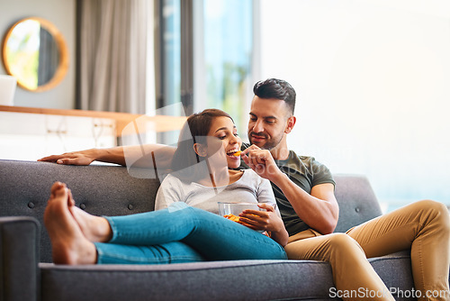 Image of Love, happy couple on sofa and eating chips in living room of their home. Caring or bonding together, relaxing or comfortable and happy married people on couch watching television for quality time.