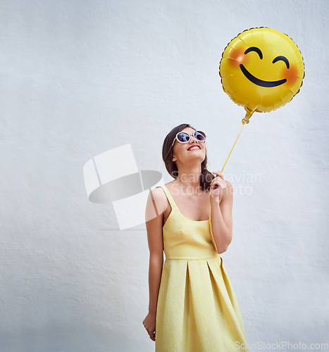 Image of Woman, balloon and happy by wall in with emoji, smile and face for fashion sunglasses at party, event or celebration. Gen z and girl and excited with icon, space and yellow dress to celebrate spring