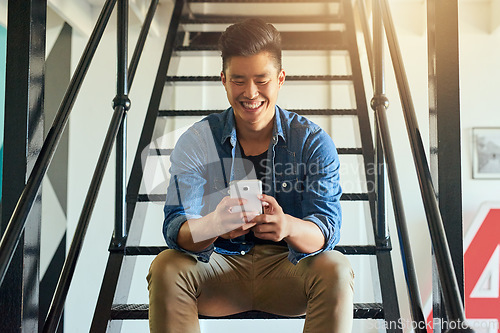 Image of Asian man, texting and office stairs with phone, smile and communication on social network app. Young japanese businessman, web design startup and relax on steps in workplace for chat with smartphone