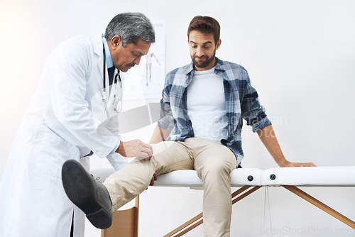 Image of Healthcare, patient with knee pain and doctor at clinic, help and wellness checkup of person at hospital. Medicine, health care expert and Indian man in doctors office consulting medical professional