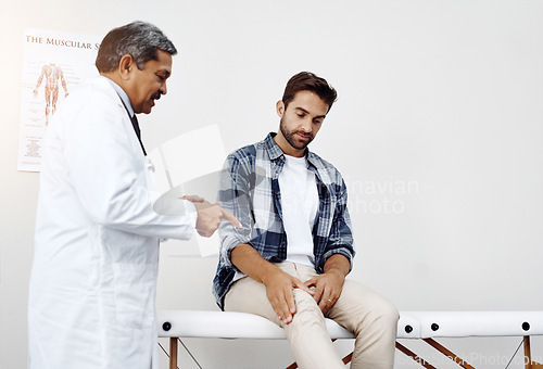 Image of Healthcare, doctor and patient with knee pain in consultation for expert advice, information and discussion. Medicine, health care and Indian man in doctors office consulting medical professional.