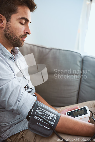 Image of Hypertension, stress and man test blood pressure in a home sofa or living room for medical or health exam. Monitor, reading and man with equipment or machine for chronic disease in a house