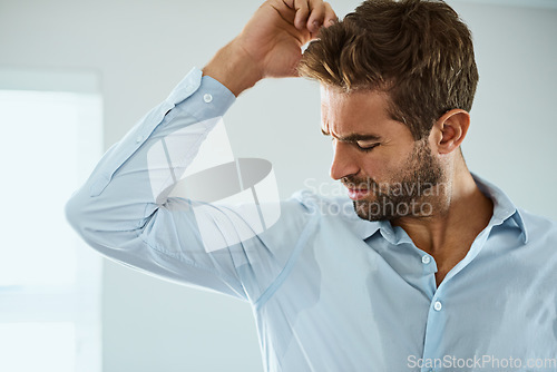 Image of Shirt, stress with man smelling armpit sweat stain and indoors at his home. Hygiene or hyperhidrosis, deodorant protection for sweaty mark on clothing and young male person sweating with wet spot