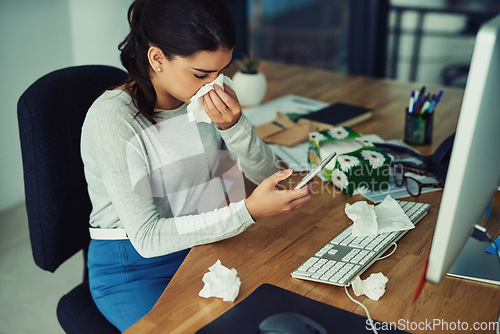Image of Blowing nose, phone and a business woman working at her desk in the office while sick, ill or unwell. Covid, tissue and allergies with a young female employee typing a mobile text message at work