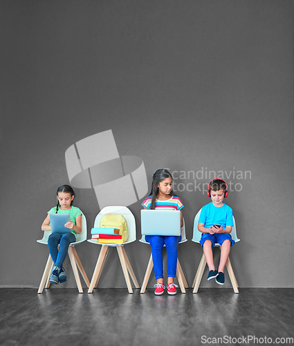 Image of Children, chair and technology for learning and education while online for research on internet. Kids or students against a grey mockup wall with laptop, tablet and phone in a waiting room with space