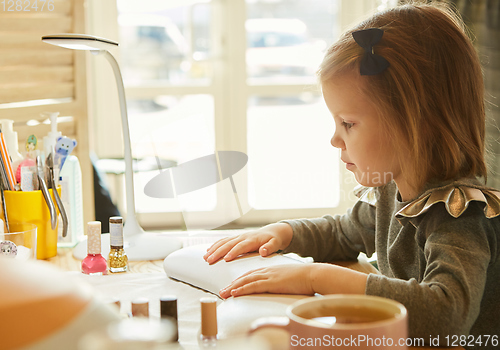 Image of Little girl in nail salon receiving manicure by beautician. Little girl getting manicure at beauty salon.