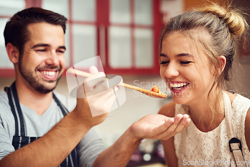 Image of Food, man feeding a woman with spoon and in a kitchen of their home. Hungry or happiness, healthy relationship and happy people cooking preparing meal for lunch or dinner time in their house