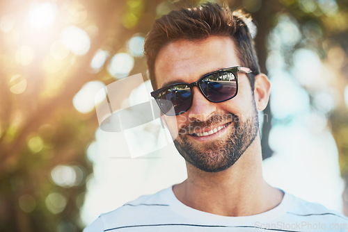 Image of Sunglasses, casual and portrait of a happy man in an outdoor park while on a vacation, adventure or holiday. Smile, confidence and young male person with eyewear standing in a garden on weekend trip.