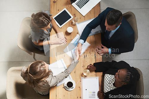 Image of Business people, handshake and meeting with documents above for hiring, partnership or collaboration at the office. Top view of businessman shaking hands for recruiting, teamwork or marketing project