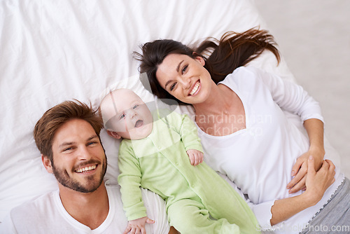 Image of Top view, portrait and happy parents with baby on bed for love, care and quality time together at home. Smile of mother, father and family with cute newborn kid relaxing in bedroom, fun and happiness