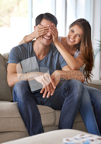 Image of Portrait, couple and surprise with hands cover eyes for happy reveal in home living room or woman, sitting together with partner on sofa. Girl, man or playing, guess who for excited announcement