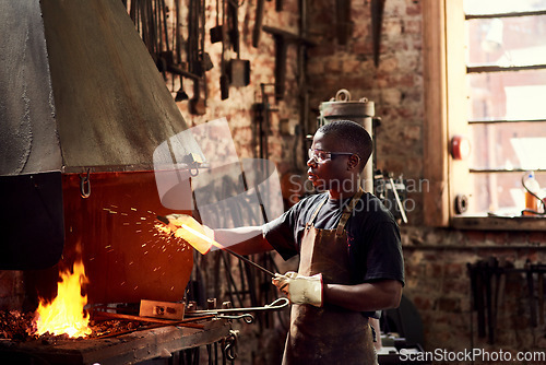 Image of Blacksmith, fire and a black man welding metal in a workshop for manufacturing or industrial design. Factory, melting or industry with a male welder in metalwork using a hot flame to melt material