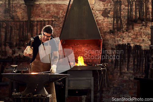 Image of Blacksmith, forge and man in metal workshop and manual working on hot steel with hammer, sparks and fire. Master, welding job or iron tools manufacturing and expert, trade and dark workspace