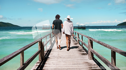 Image of Travel, freedom and rear view of couple at beach walking, holding hands and relax on ocean jetty with blue sky background. Summer, holiday and behind man with woman at sea, traveling or Bali romance