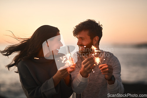 Image of Love, beach and couple with sparklers for celebration, party and quality time on romantic date. Nature, sunset and happy man and woman with fireworks for honeymoon on holiday, weekend and vacation