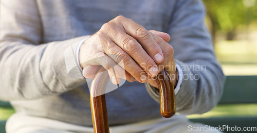 Image of Closeup of senior hands on a walking cane for help, assistance or healthcare in outdoor park. Nature, retirement home and zoom of elderly male person with disability sitting in garden with wood stick