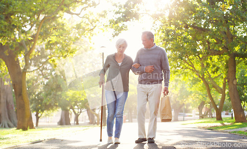 Image of Senior couple, cane and walking outdoor at a park with a love, care and support for health and wellness. A elderly man and woman in nature for a walk, quality time and healthy marriage or retirement